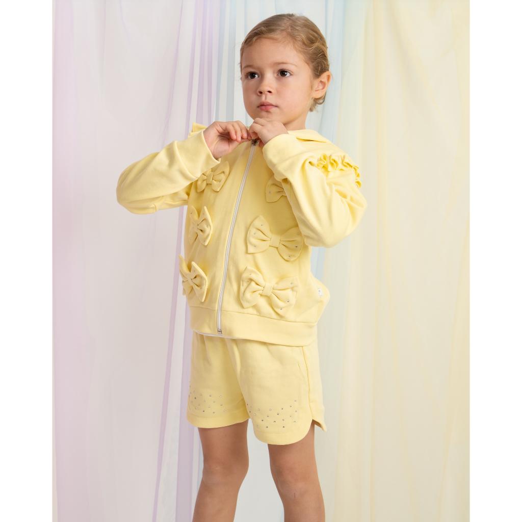 Young girl wearing a yellow outfit with decorative elements against a light curtain background