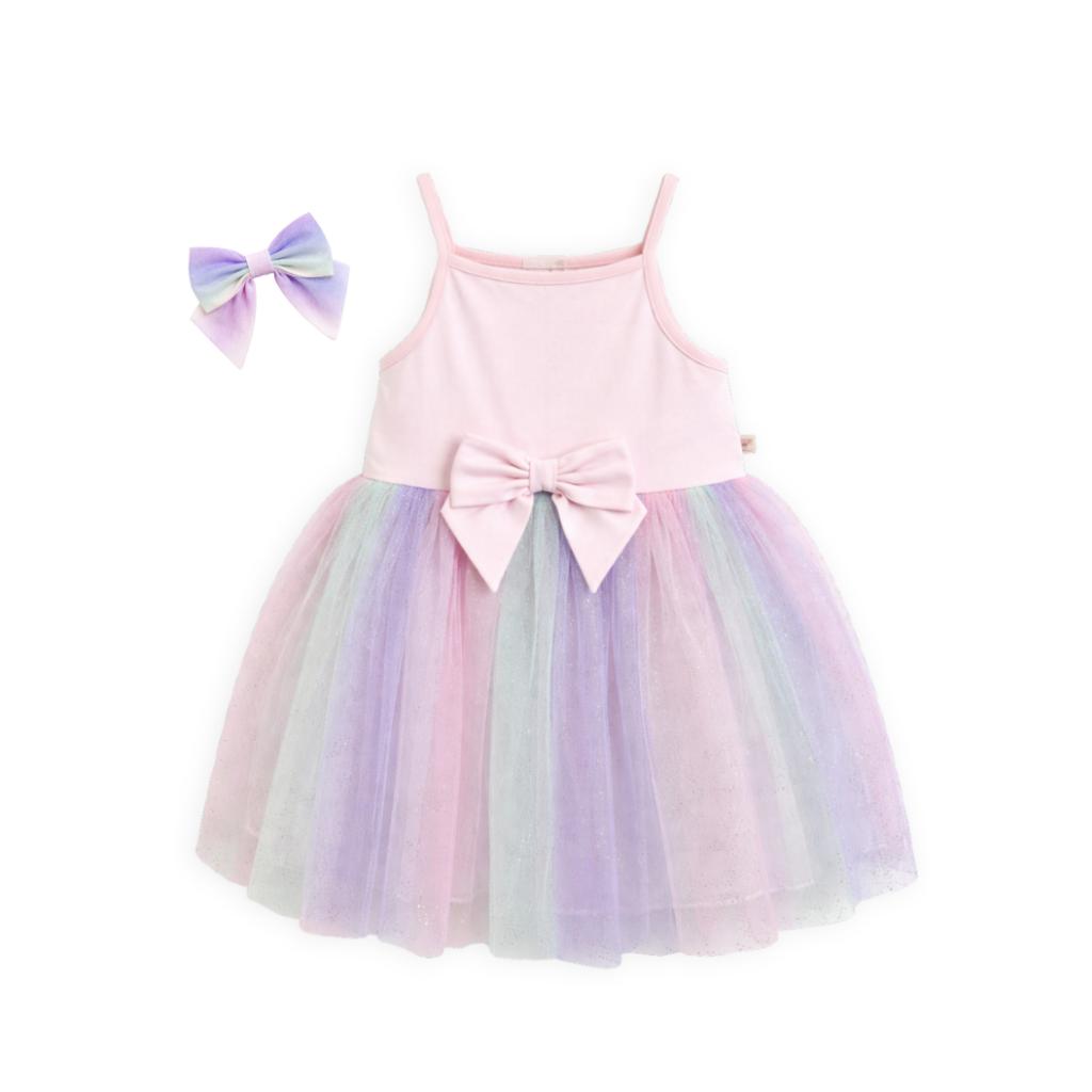 Caramelo rainbow pastel dress features a soft pink bodice with delicate straps and a statement bow at the waist, paired with a layered rainbow‑tulle skirt for a magical, floaty finish.