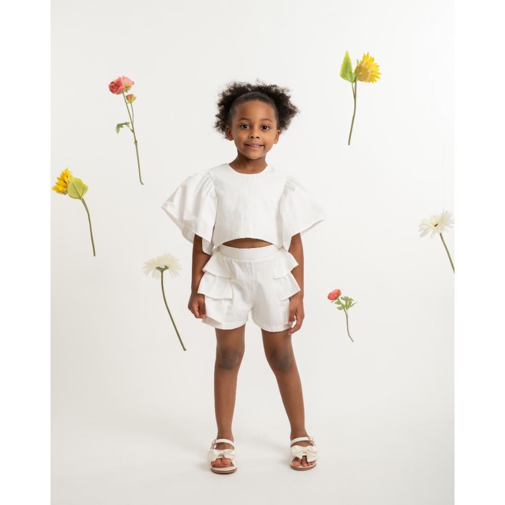 Model wearing a Caramelo white ruffle short set with statement back bow and matching layered‑ruffle shorts. A soft, elegant summer outfit for girls