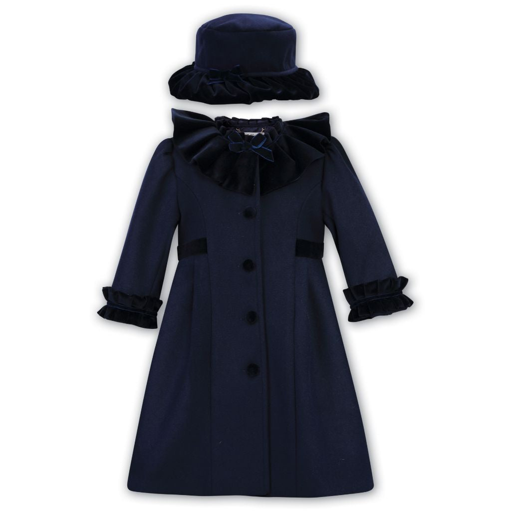 A navy coat for children with velvet covered buttons and a velvet ruffle to the collar and cuffs, accompanied by a matching hat.